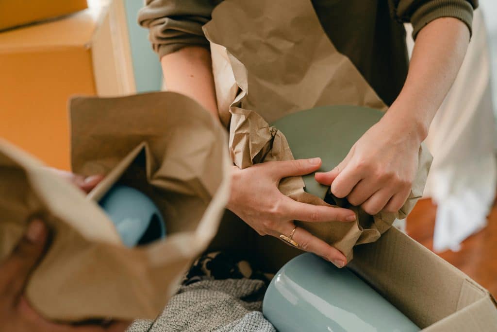 A mans hands wrapping up vases with brown paper to pack