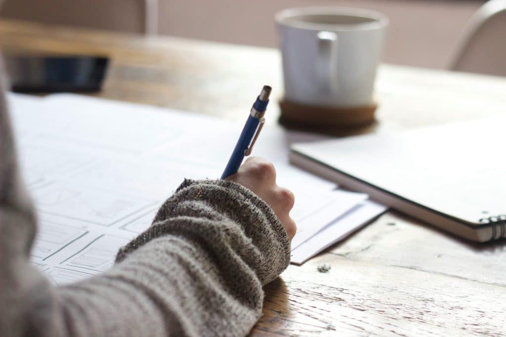 Hand of woman writing on paper on a desk with a mug on the table