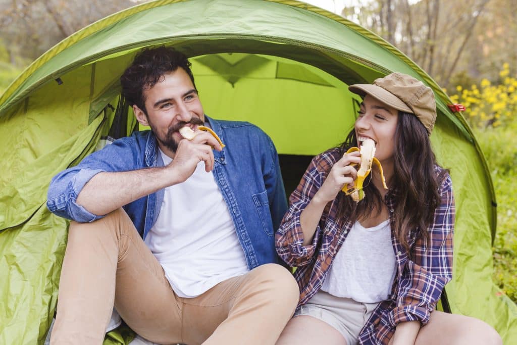 A man and a woman sitting inside a green tent eating bananas