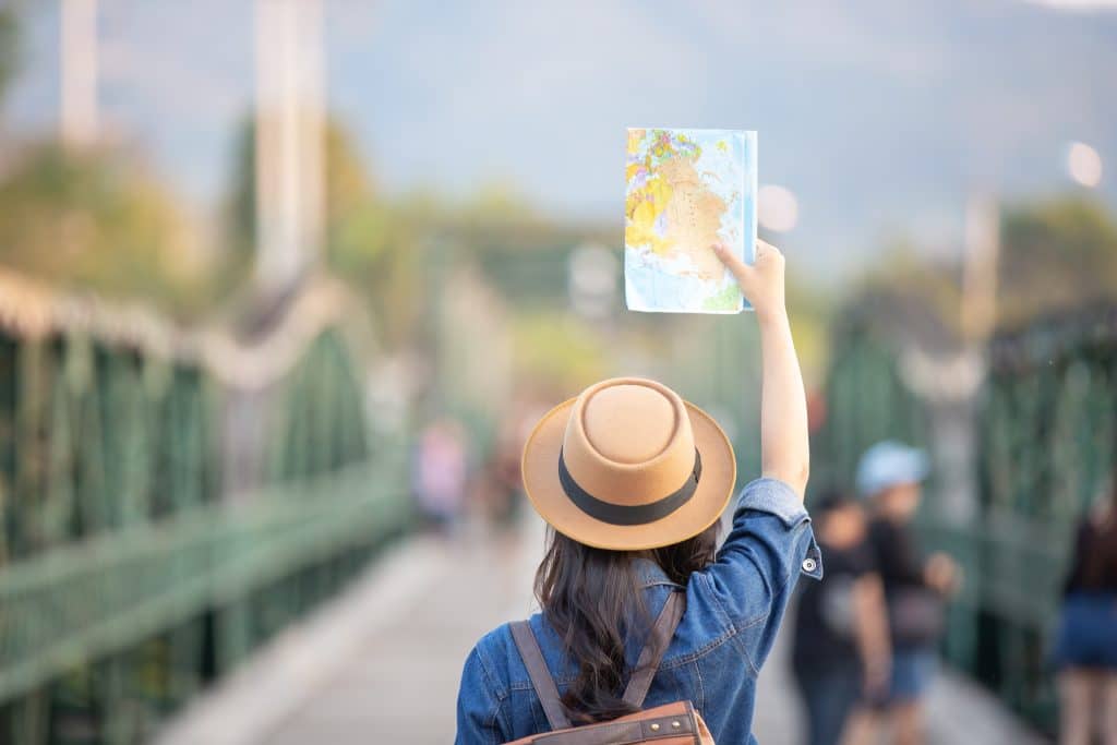 Woman with her back to the camera holding up a map and facing a bridge