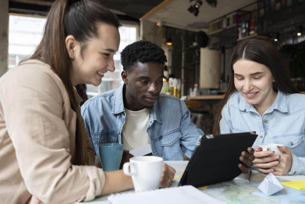 One man and two women sitting at a table looking at an ipad and drinking coffee