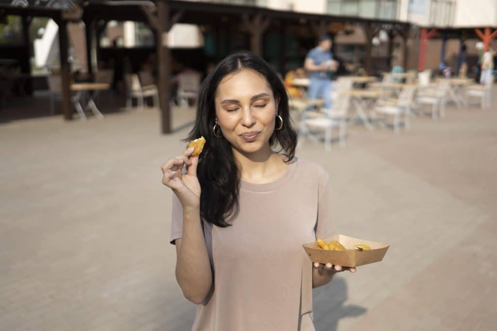 Woman standing up holding a container of food and eating from it