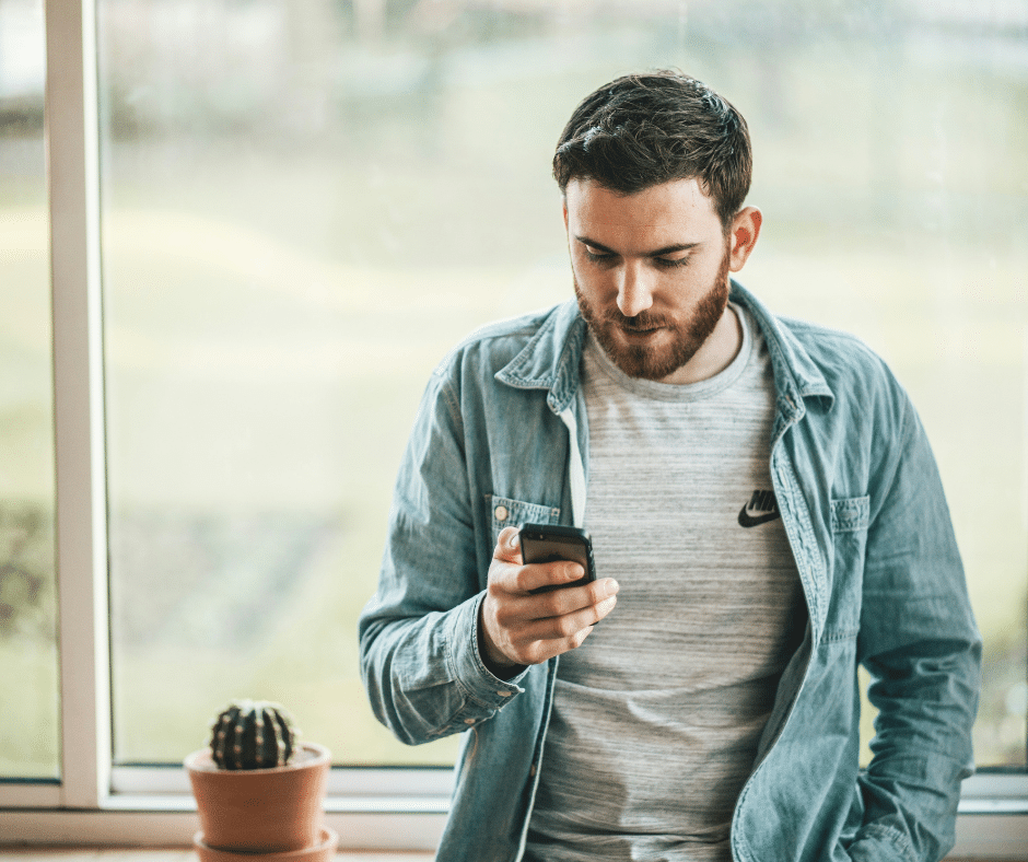 A young man leaning against a bench looking at his phone