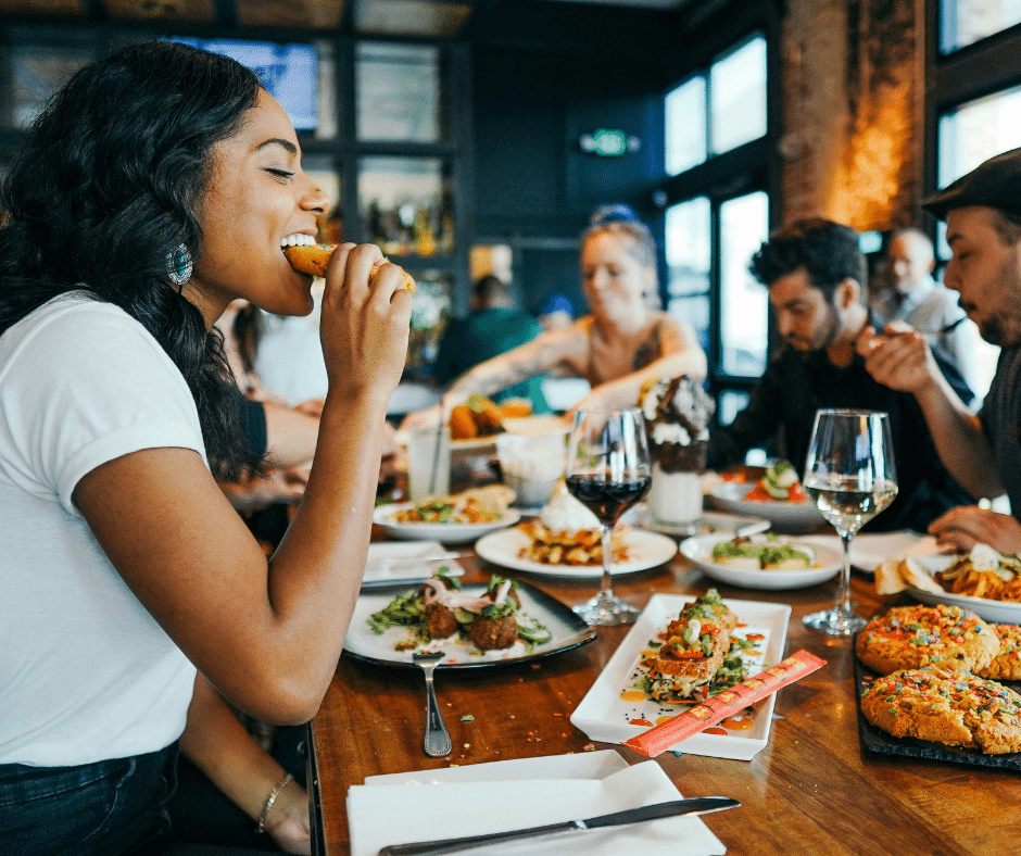 A girl with a groups of friends at a restaurant enjoying what she is eating